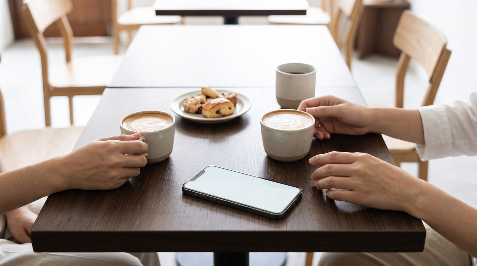 カフェのテーブルに置かれたスマートフォンと、両側から伸びる手